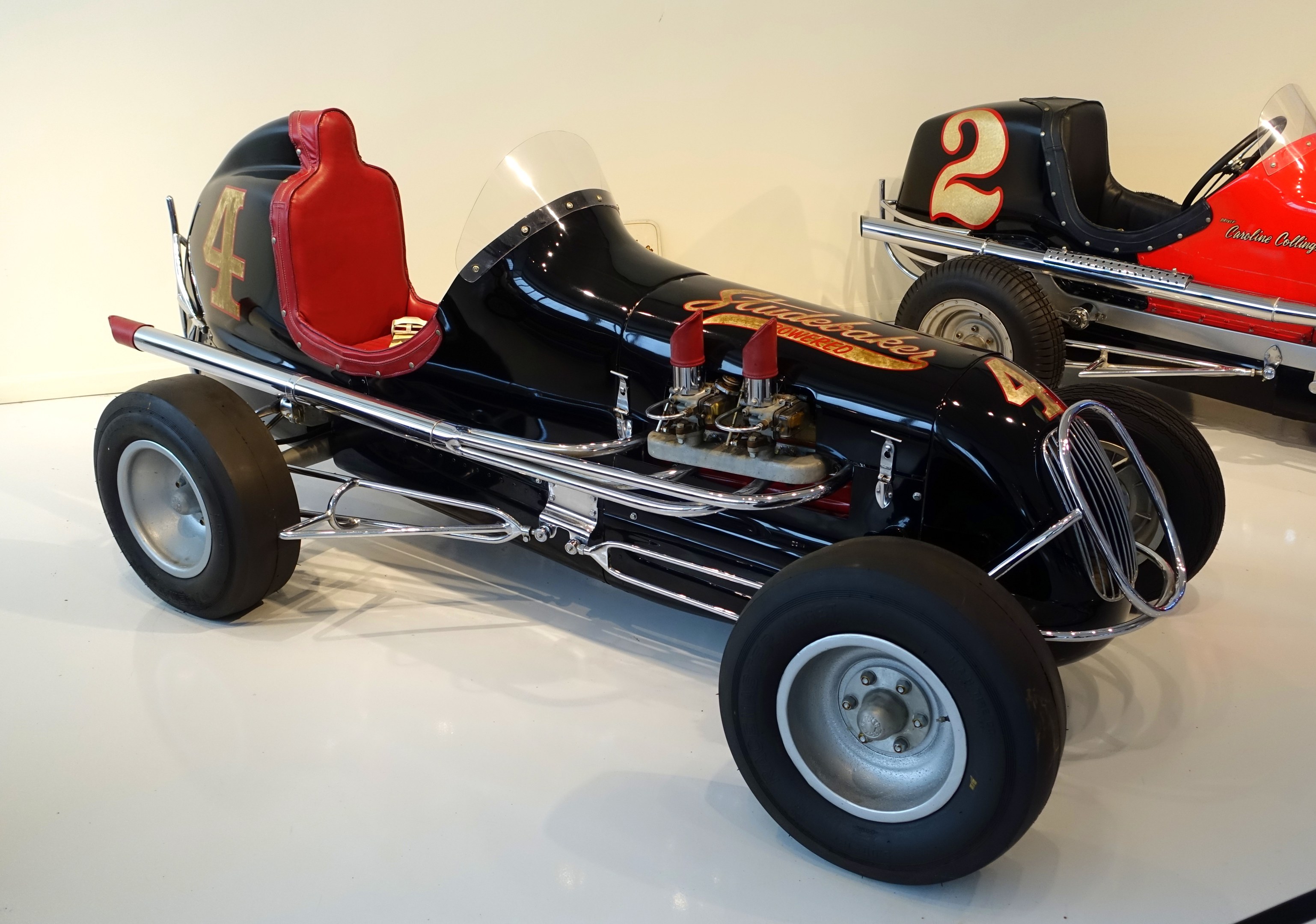 Zwei Oldtimer-Rennwagen in einem Museum ausgestellt, auf dem Boden stehend mit einer Wand im Hintergrund.