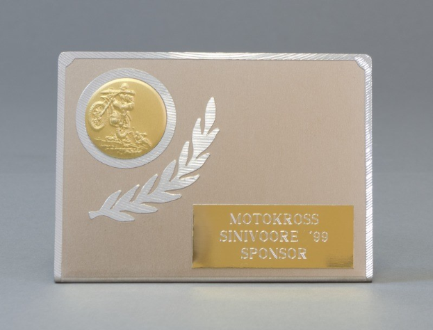 Eine goldene und silberne Visitenkarte mit einem Lorbeerkranz-Design, mittig im Bild mit Text, der wahrscheinlich den Namen des Sponsors angibt.