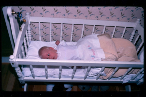 Ein Baby in einer Wiege, das mit einer Decke bedeckt ist, mit W√§nden und Boden im Hintergrund.