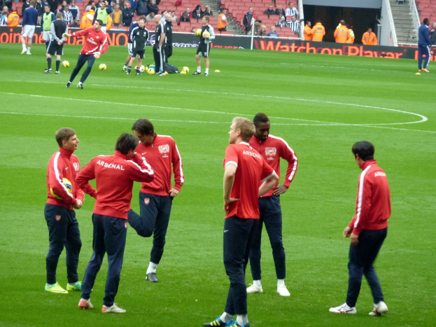 Eine Gruppe von Spielern, die auf einem grünen Feld mit Fußballen stehen und ein Publikum im Hintergrund auf Stühlen sitzt.