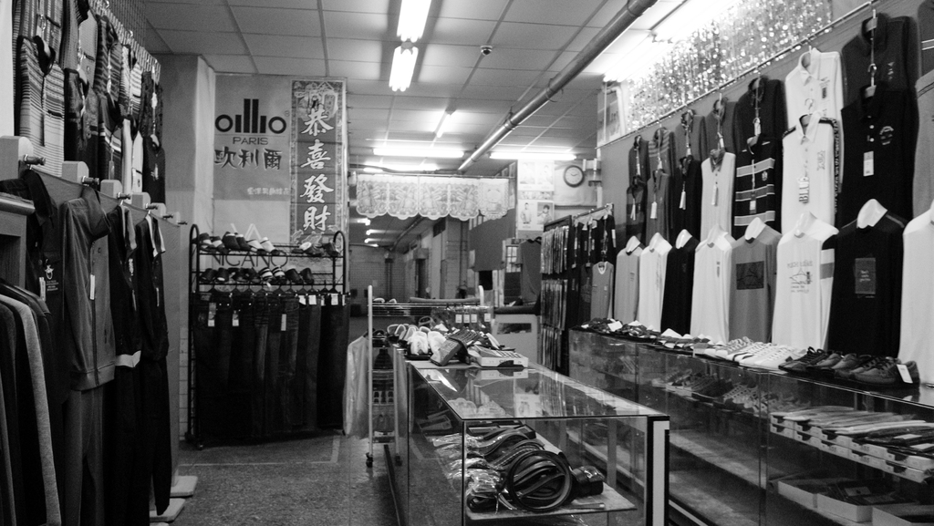 Eine Anzeige Von Kleidung, Gürteln Und Schuhen Mit Einer Uhr An Der Wand, Hängender Stoff, Lampen Und Ein Banner Mit Text Auf Der Linken Seite.