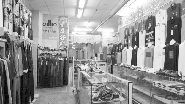 Eine Anzeige Von Kleidung, Gürteln Und Schuhen Mit Einer Uhr An Der Wand, Hängender Stoff, Lampen Und Ein Banner Mit Text Auf Der Linken Seite.