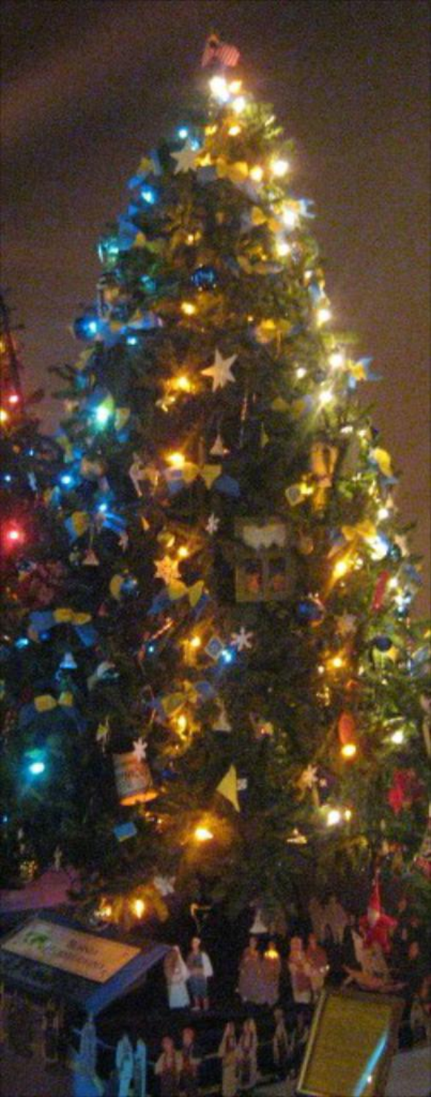 Ein geschmückter Weihnachtsbaum mit darunter platzierten Statuen von Menschen auf einem Tisch.