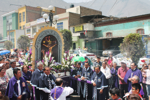 Menschen auf einer Straße mit einem Kreuz und Blumensträußen in der Mitte, Autos im Hintergrund und Gebäuden, Bäumen und Straßenlaternen.