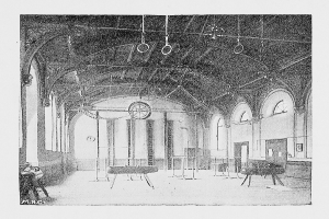 Schwarzes und weißes Foto eines großen Turnhallen mit Tischen, Stühlen, Säulen, Wänden, Fenstern und Deckenringen beschriftet mit "New York City Gymnasium".