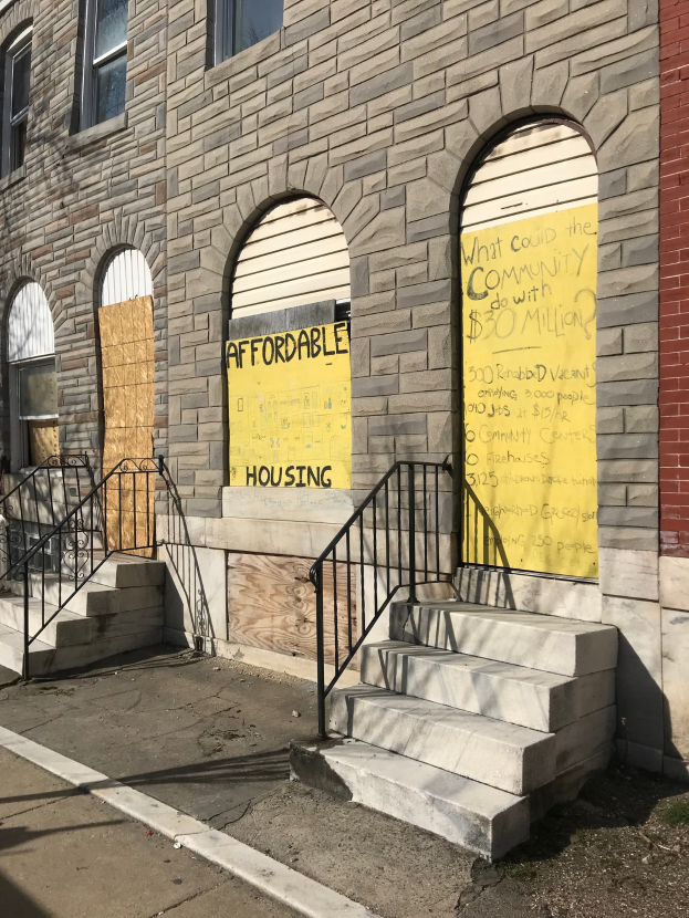 Verschaltes Gebäude mit "Bezahlbarer Wohnraum"-Schilder, Treppe mit Geländer und Straße unten.