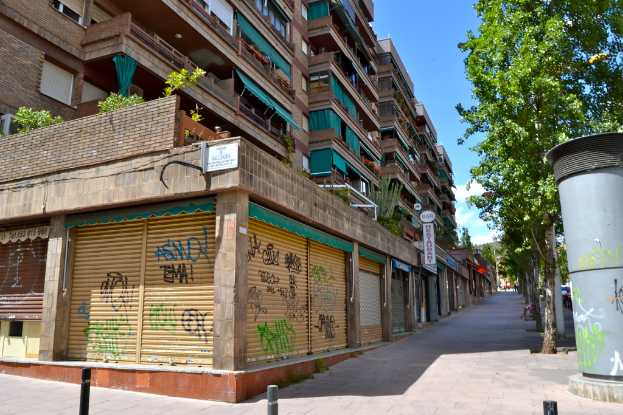 Eine Szene mit mehreren Gebäuden mit Fenstern, grüner Kleidung, Geschäften, Schildern und umgebenden Bäumen und Pflanzen.