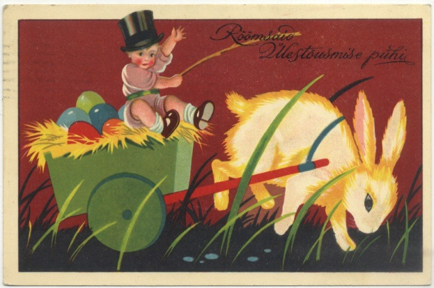 Eine alte Postkarte mit einem Baby in einem Zylinder, das einen mit bunten Ostereiern gefüllten Handkarren schiebt, begleitet von einem Kaninchen, mit handgeschriebenen Ostergrü├čen.