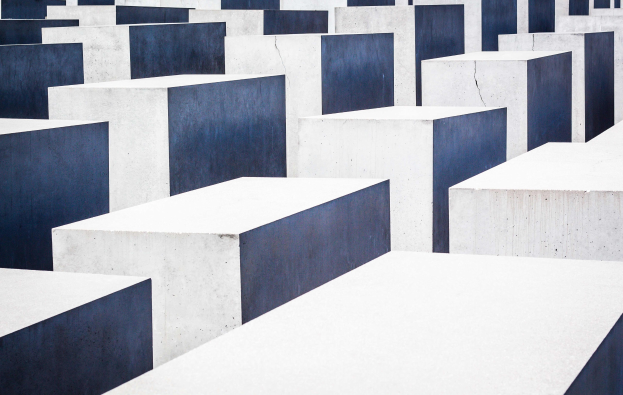 Luftaufnahme des Holocaust-Mahnmals für die ermordeten Juden Europas in Berlin, mit zahlreichen weißen und blauen Betonsteinen in einem Gittermuster.