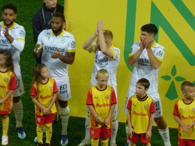 Eine Gruppe von Fußballspielern in Uniformen klatscht auf einem Ligue-1-Feld in celebration, mit einem "Ligue-1"-Schild im Hintergrund.