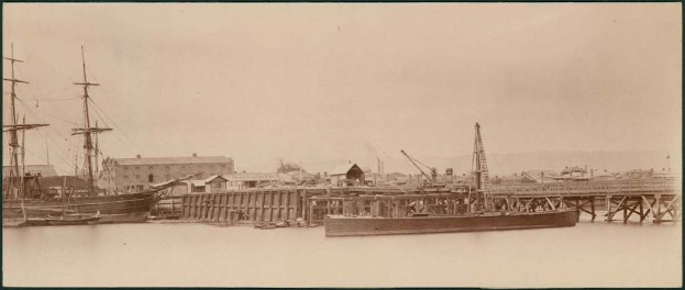 Eine Szene mit Wasser, Booten, Gebäuden, Strommasten und einem Himmel im Hintergrund.
