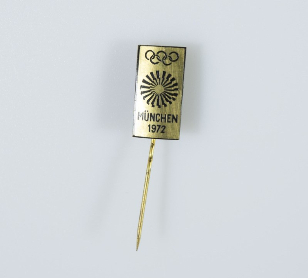 Goldene Nadel mit "München 1972 Olympische Spiele" Text auf einem weißen Hintergrund.