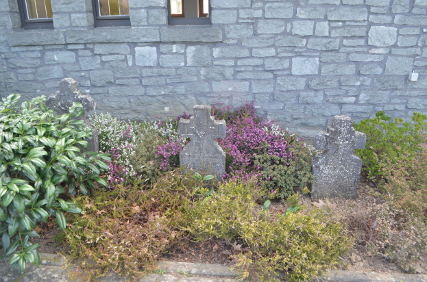 Steinbau mit Garten, der Pflanzen, Blumen und Grabsteine vor dem Gebäude zeigt, Fenster im Gebäude sichtbar