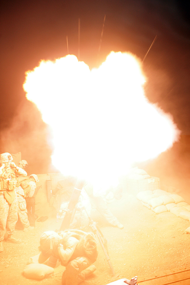 Mehrere Personen in Uniformen und Helmen auf einem Gelände mit verstreuten Taschen, mit einem Feuer in der Mitte.