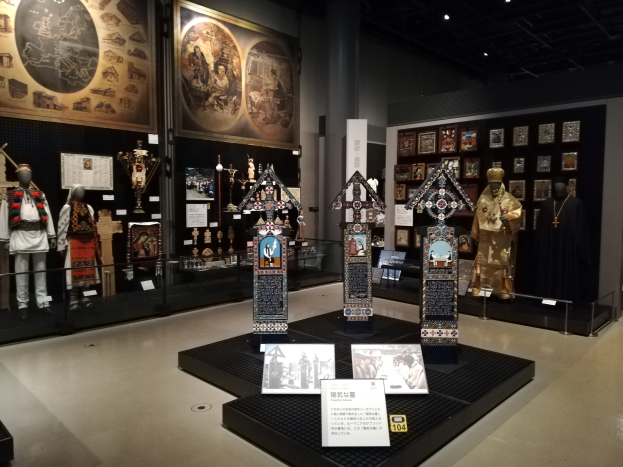 Ein Museumsraum mit verschiedenen Gegenständen, darunter Schaufensterpuppen in Kostümen, Fotorahmen an den Wänden, einer Säule und Deckenleuchten, gewidmet der Geschichte Japans.