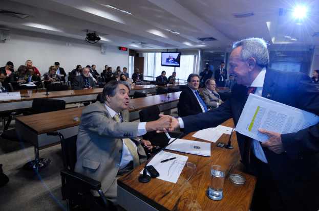 Eine Gruppe von Menschen ist in ein Gespräch mit einigen im Hintergrund sitzenden Personen vertieft, unter einer Decke mit Leuchten, wie auf einem Fernsehbildschirm zu sehen.