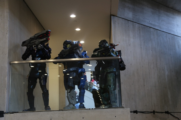 Drei Spielzeuge mit Waffen stehen unter einem weißen Dach mit Lichtern, mit Wänden auf beiden Seiten und Menschen im Hintergrund.