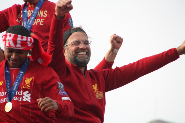 Liverpool-Trainer Jürgen Klopp feiert mit seinen Spielern nach dem Gewinn der UEFA Champions League, umgeben von zwei medaillentragenden Personen, mit dem Himmel im Hintergrund.