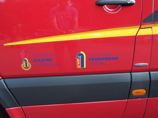 Roter Lieferwagen mit einer gelben Streifen, Türgriff, Schildlogo mit einem Löwen in einem Lorbeerkranz und der Aufschrift "Deutscher Jugendfeuerwehrverband".