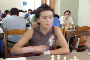 Ein Raum mit Menschen an Tischen beim Schachspielen, mit einer Vorhangwand und einem Foto in der Ecke.