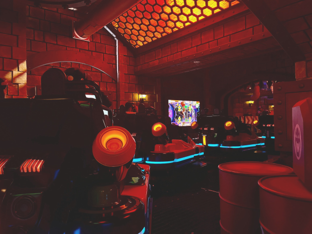 Ein hell erleuchteter Raum voller verschiedener Arcade-Videospielautomaten, Bildschirme und Gegenstände, einschließlich einer sichtbaren Röhre und Deckenlampen.