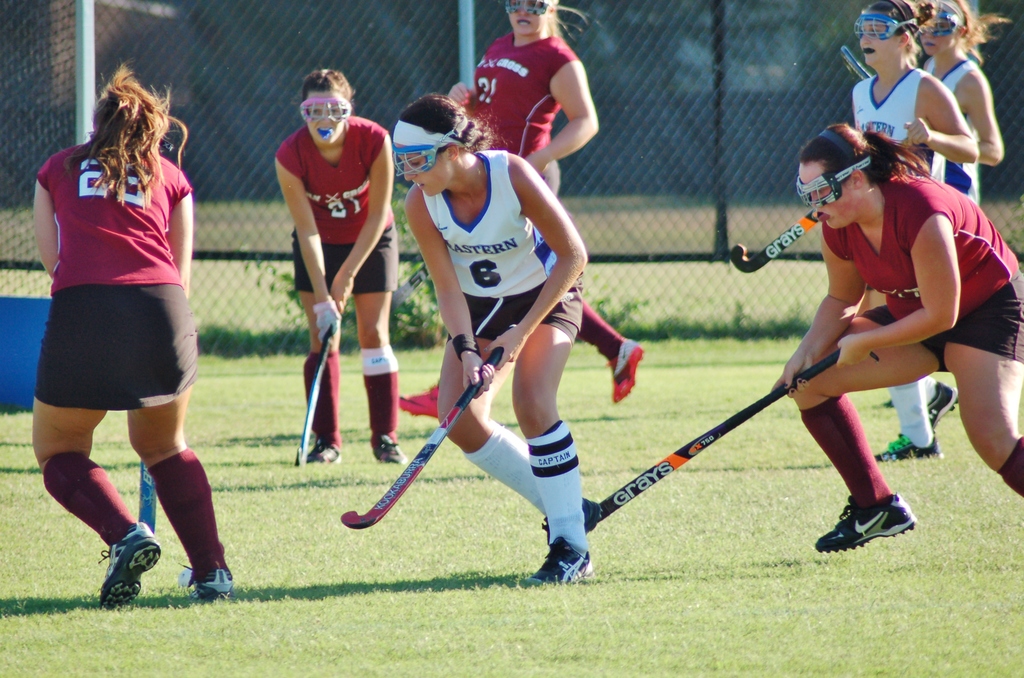 Frauen spielen Hockey auf einem Rasenfeld mit einem Netz als Hintergrund.