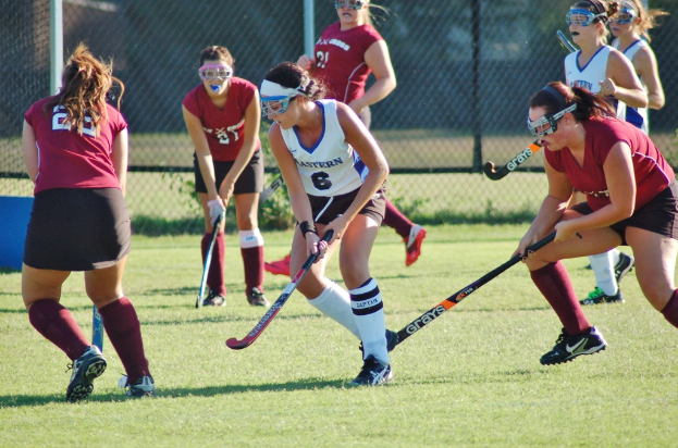 Frauen spielen Hockey auf einem Rasenfeld mit einem Netz als Hintergrund.