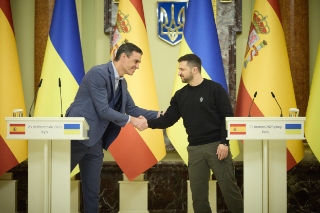 Zwei Männer, der ukrainische Premierminister Viktor Janukowytsch und der ukrainische Präsident Petro Poroschenko, schütteln sich die Hände vor einem Hintergrund aus Flaggen, mit Mikrofonen und Tafeln auf den Podien, einem Logo an der Wand und beleuchteter Szene.