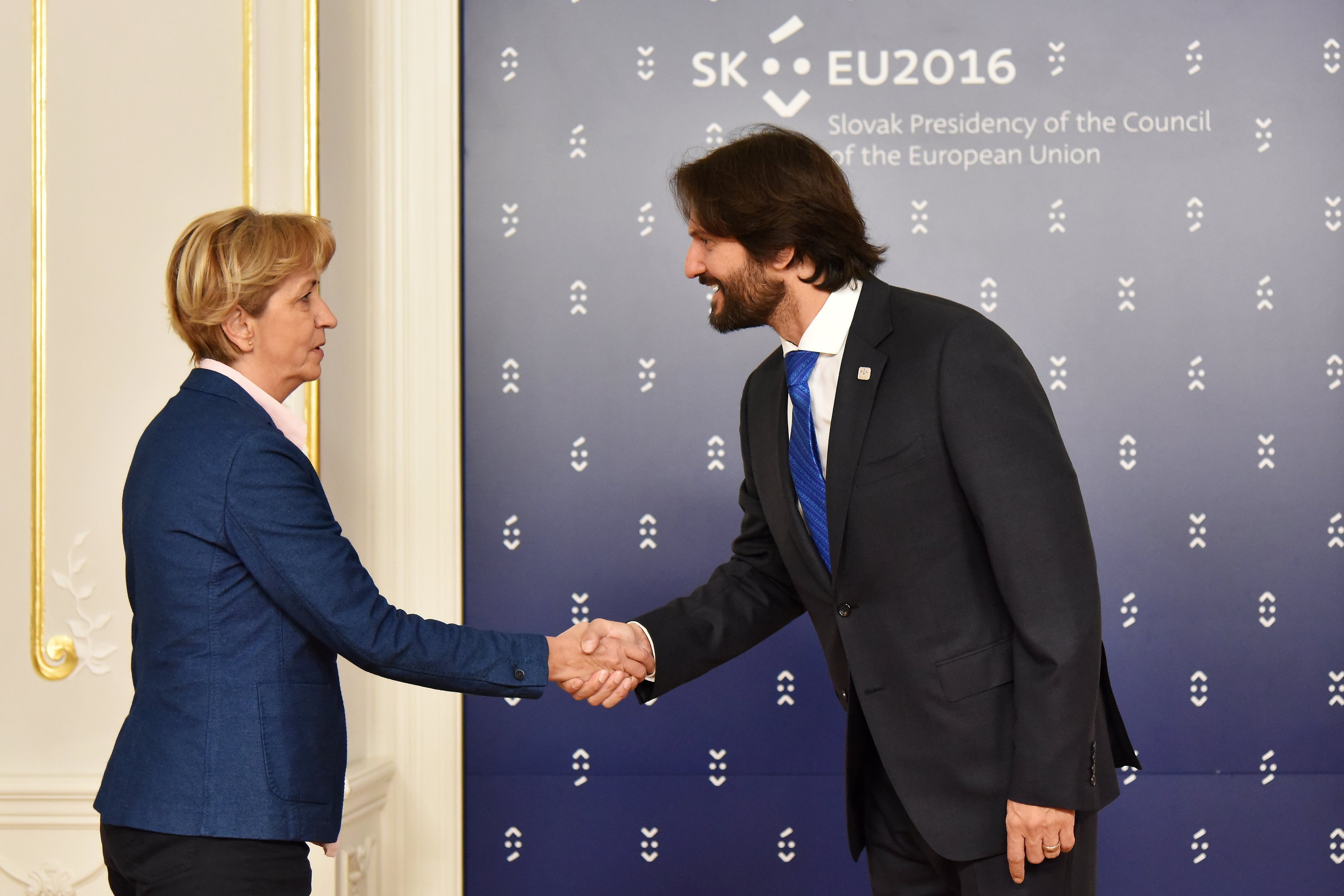 Bundeskanzlerin Angela Merkel und Bundespräsident Joachim Gauck schütteln sich die Hände vor einer Wand mit einem "EU-Gipfel"-Plakat und einer Tür im Hintergrund, beide lächeln.