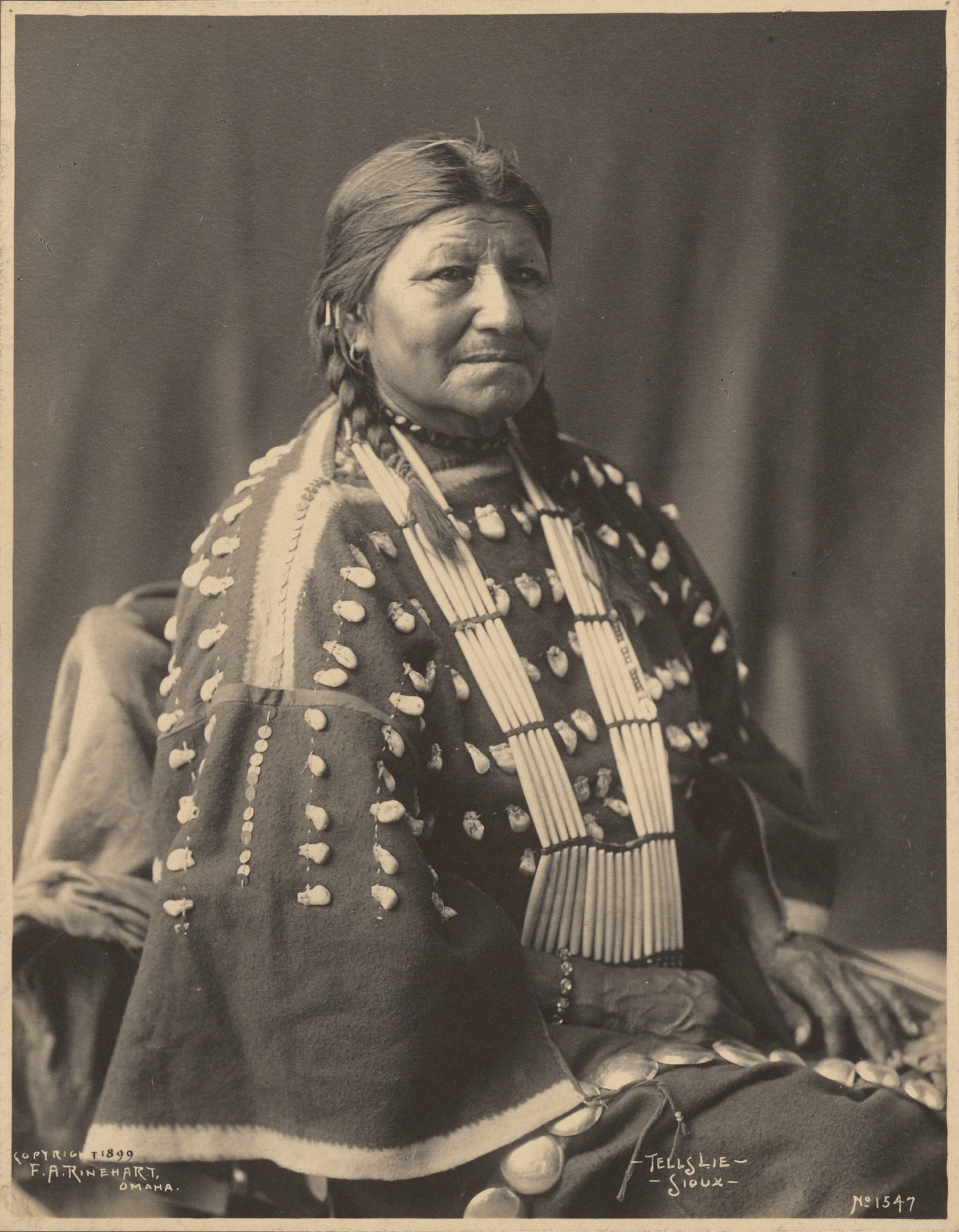 Altes Schwarz-Weiß-Foto einer indischen Frau in traditioneller Kleidung mit ernstem Gesichtsausdruck, gefalteten Händen, zurückgebundenem Haar und einer Federhaube.