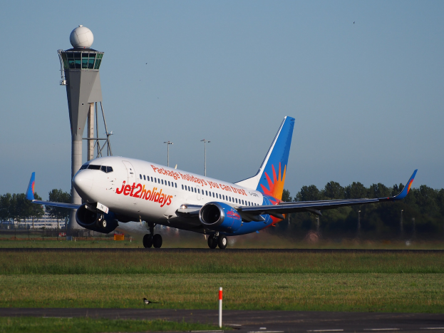 Jet2holidays Airbus A320-200 startet von Frankfurt Airport mit saftig grünem Gras, einem hohen Turm, Bäumen, Gebäuden und einem hellblauen Himmel mit Sonne.