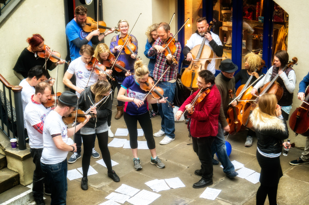 Eine Gruppe von Menschen, die Geigen spielt, mit verstreuten Papieren auf dem Boden.