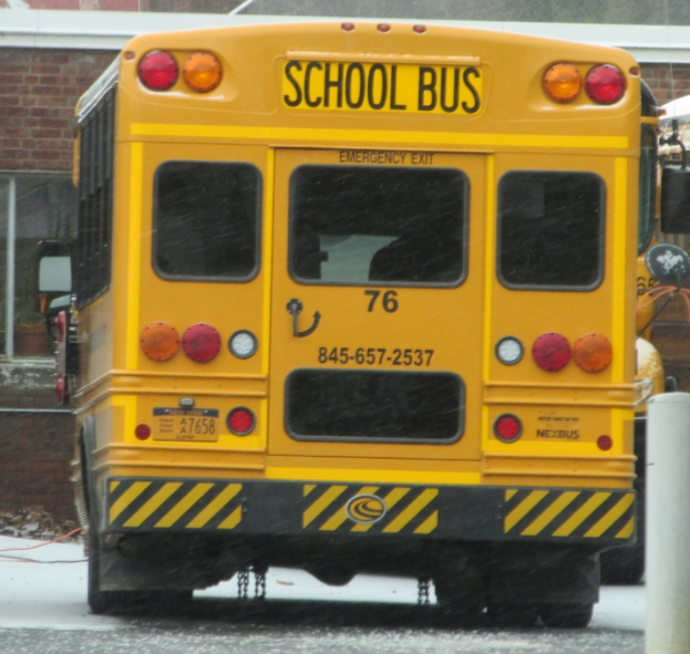 Ein gelber Schulbus mit der Aufschrift "Schulbus", der vor einem Backsteingebäude mit Fenstern geparkt ist.