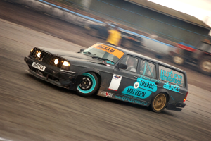 Ein Auto fährt eine Rennstrecke entlang mit einem Fahrer drin, umgeben von anderen Fahrzeugen, mit einem unscharfen Hintergrund, der hohe Geschwindigkeit andeutet.