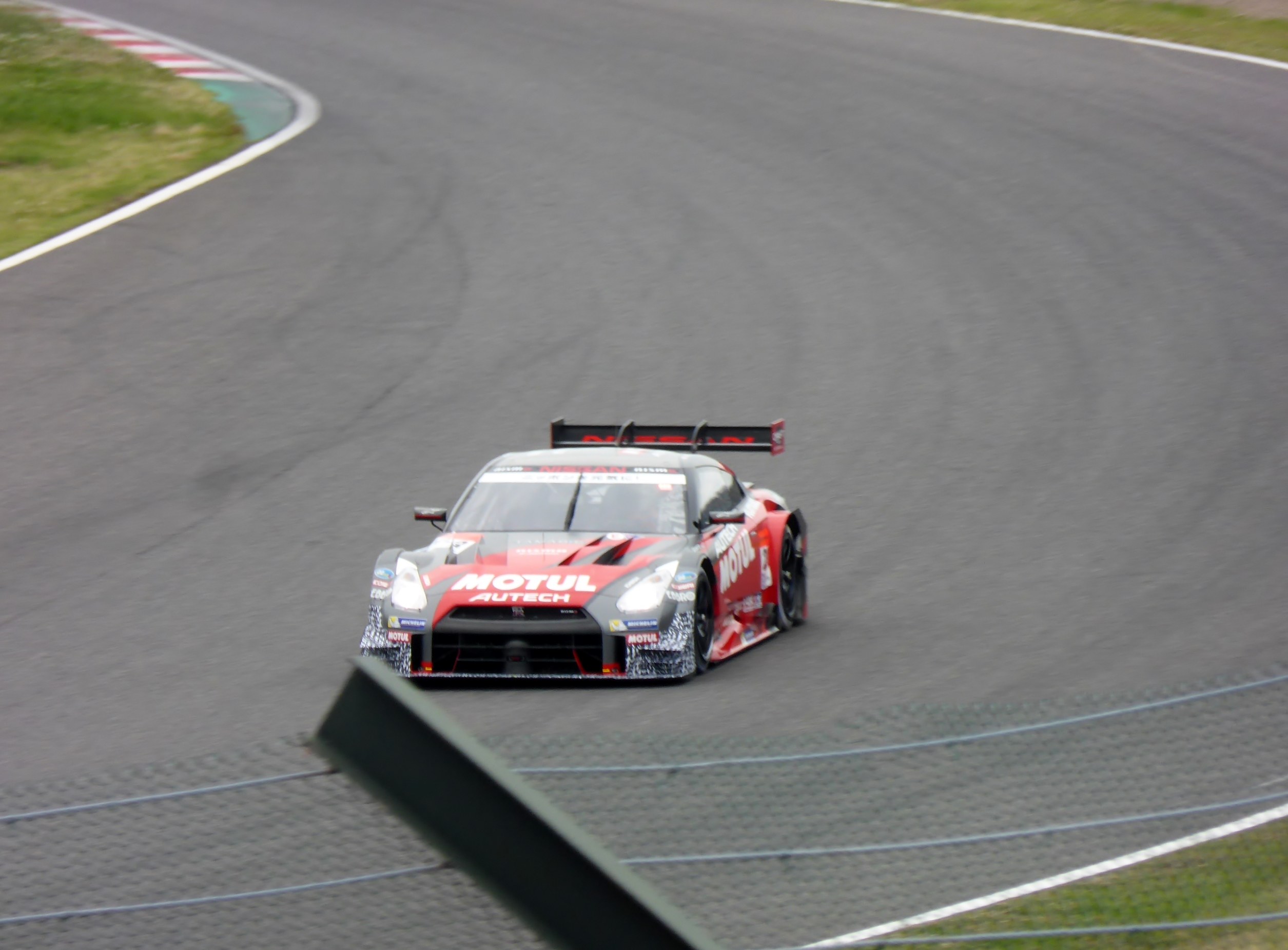 Nissan GT-R Nismo GT3 Rennauto auf der Nürburgring 24 Stunden Strecke, flankiert von grünem Gras.