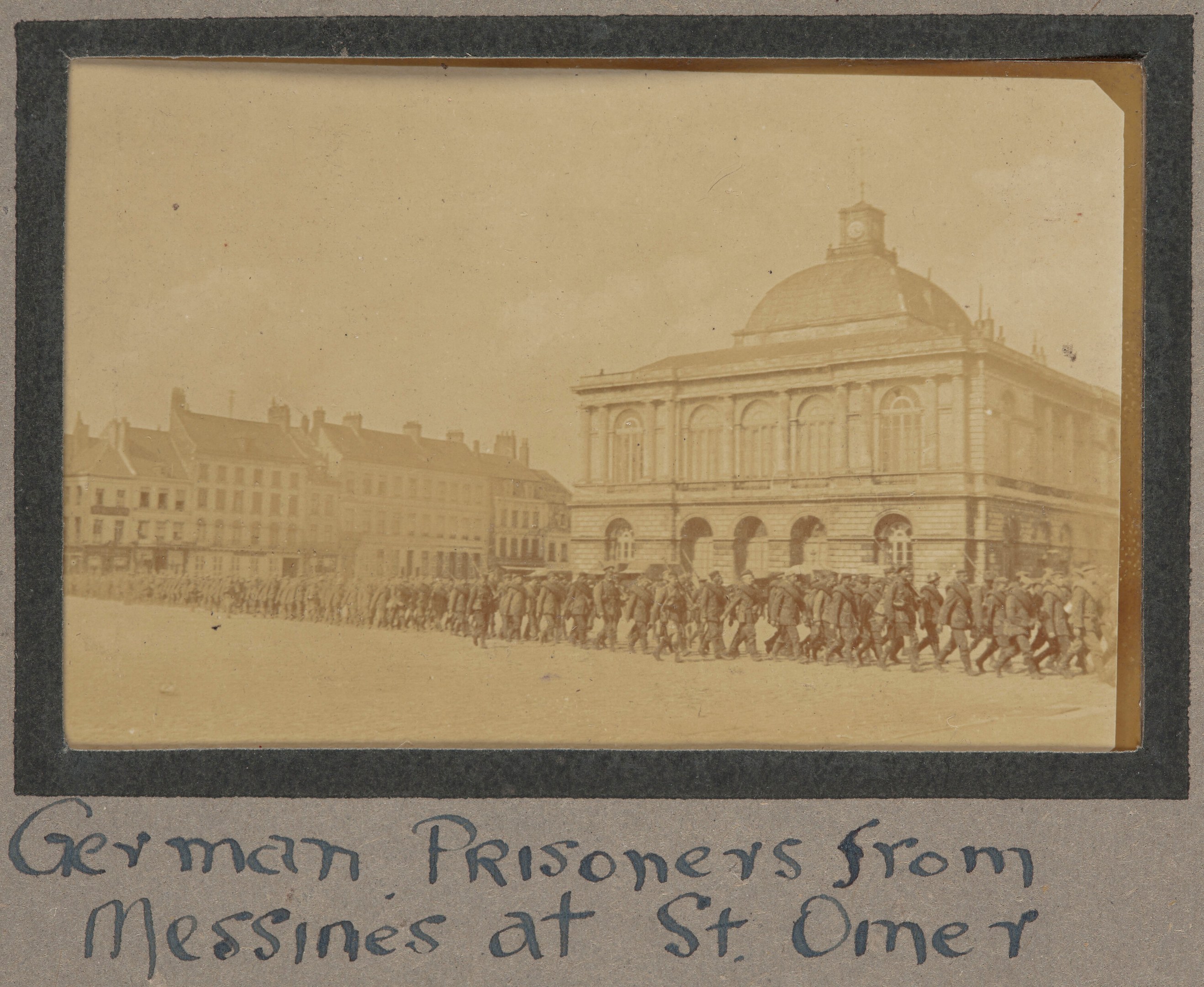 Deutsche Kriegsgefangene aus Messines vor einem Gebäude mit einem klaren blauen Himmel im Hintergrund, mit Text unten.