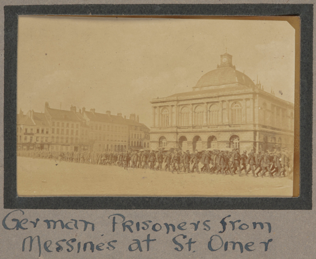 Deutsche Kriegsgefangene aus Messines vor einem Gebäude mit einem klaren blauen Himmel im Hintergrund, mit Text unten.