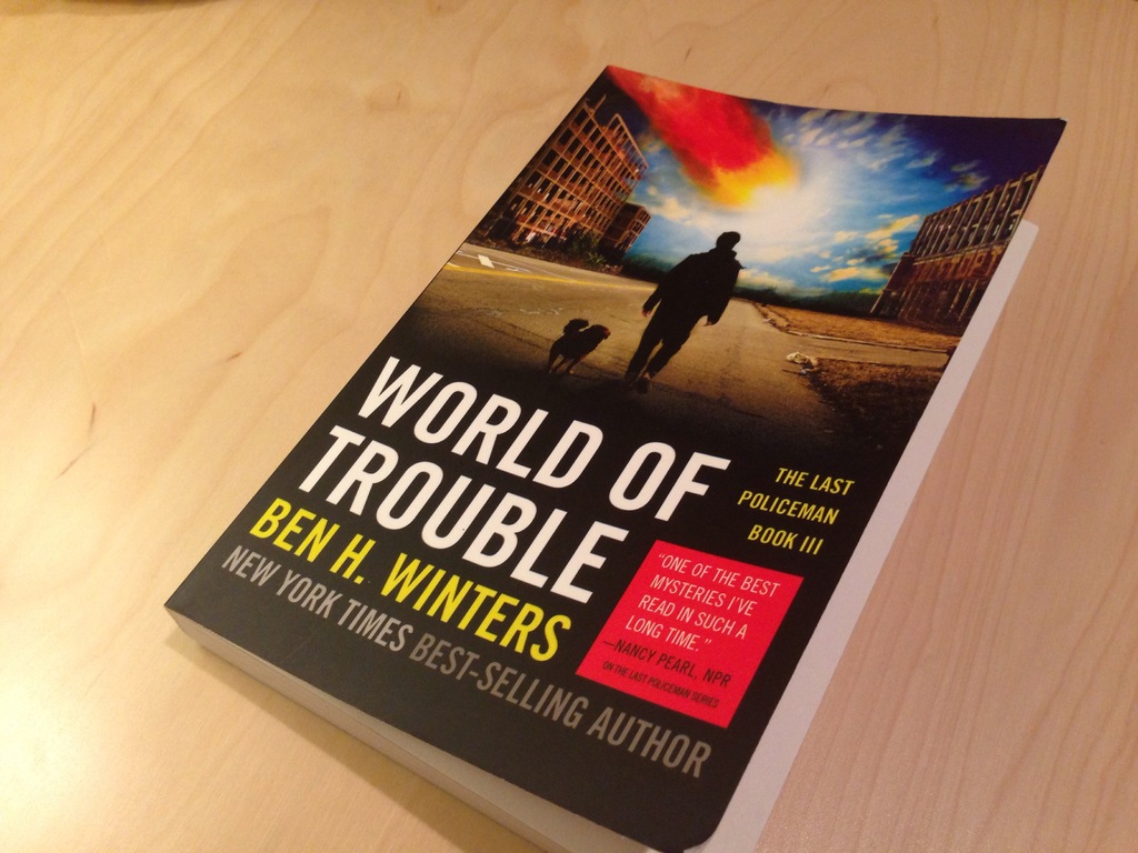 Ein Buch mit dem Titel "World Of Trouble" mit einem Bild eines Mannes und eines Hundes auf einem Tisch.