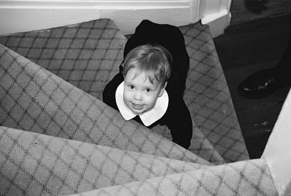 Ein Kind sitzt auf einer Treppe mit Schuhen rechts in einem Schwarz-Weiß-Bild.