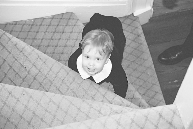 Ein Kind sitzt auf einer Treppe mit Schuhen rechts in einem Schwarz-Weiß-Bild.