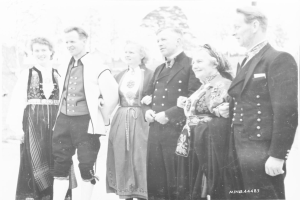 Eine Gruppe von Menschen in Schwarz-Weiß-Kleidung, die gemeinsam vor Bäumen im Freien lächeln, mit Text unten: "Bayerische Familie in den 1930er Jahren".