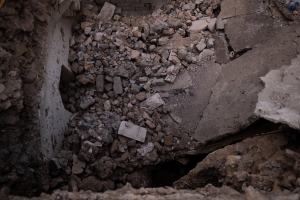 Ein eingestürztes Gebäude mit einem großen Loch im Boden, umgeben von Schutt, mit einem sichtbaren Rohr auf der linken Seite, das Erdbebenschäden anzeigt.