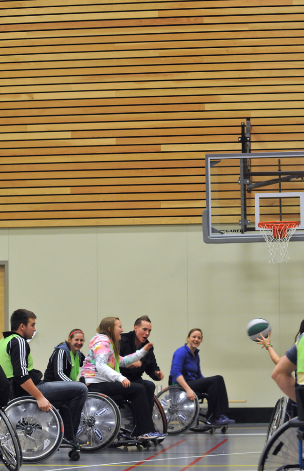 Menschen im Rollstuhl beim Basketballspielen mit einem Korb im Hintergrund.