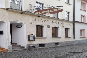Ein Gebäude mit einer Tafel, auf der "Stadt Nurnberg" steht, mit Fenstern, einer Tür und einer Treppe, die hinaufführt, sowie einem Müllcontainer im Vordergrund.