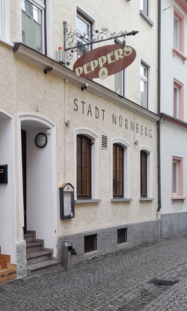 Ein Gebäude mit einer Tafel, auf der "Stadt Nurnberg" steht, mit Fenstern, einer Tür und einer Treppe, die hinaufführt, sowie einem Müllcontainer im Vordergrund.