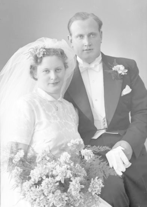 Ein Schwarz-Weiß-Foto eines lachenden Mannes und einer Frau an ihrem Hochzeitstag, die Frau hält einen Blumenstrauß und der Mann trägt einen Anzug und schaut verliebt.