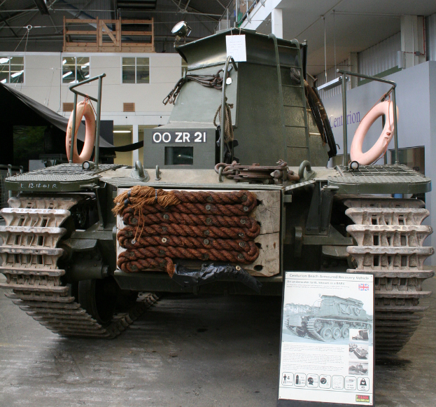 Ein Panzer-Panzer ist auf dem Boden positioniert mit einer Tafel und mehreren Bildern in der Nähe, gegen einen Hintergrund mit einer Wand, Säulen, Lampen, einem Schuppen und Stangen.