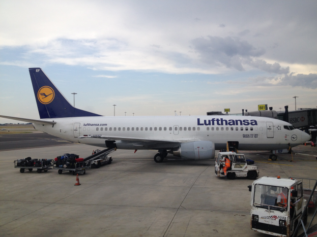 Lufthansa Airbus A320-200 am Frankfurter Flughafen mit Bodenbetriebsfahrzeugen, Wagen, Verkehrskegeln, Beschilderung und bewölktem Himmel im Hintergrund.