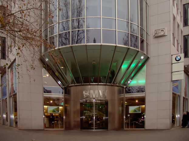 Moderner BMW-Hauptsitz mit Glasfassade in Frankfurt, Deutschland, mit Menschen vor dem Gebäude und einem Baum links daneben.