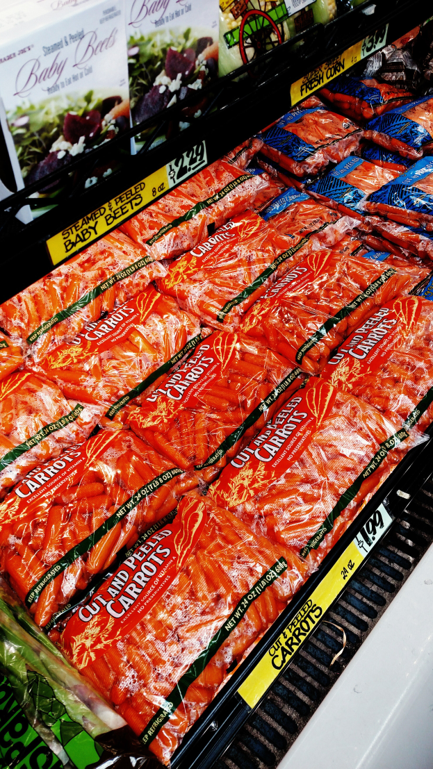 Eine Gemüsevitrine im Supermarkt mit verschiedenen Lebensmitteln, darunter Gemüsepackungen mit Preisschildern.